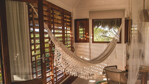 A hammock in a room with wooden floors and a view of greenery outside. - Kitejuba Bungalows (Camocim)