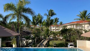 A swimming pool with palm trees and a building with a red roof in the background. - Just right (Puerto Plata)