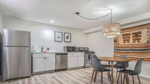 Une cuisine moderne équipée d’appareils électroménagers en acier inoxydable, une table à manger avec des chaises et un luminaire suspendu.