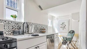 A modern kitchen with white cabinetry, a black and white patterned backsplash, a microwave, a gas stove, and a child’s high chair. - Pikes Escape! Downtown Studio w/ Arcade & Firepit (Colorado Springs)