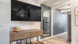 A modern living room with a flat-screen TV mounted on the wall, a wooden console table with storage, and a large mirror. - Pikes Escape! Downtown Studio w/ Arcade & Firepit (Colorado Springs)