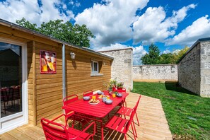 Una cabaña de madera con una mesa y sillas rojas, un ventanal pequeño y una pared de piedra.