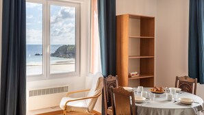 Un coin repas avec une table dressée pour deux personnes, une bibliothèque en bois et une vue sur la plage grâce à de grandes fenêtres.