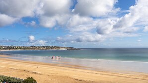 Une plage avec un ciel dégagé et quelques nuages. On aperçoit des bâtiments au loin, le long de la côte.
