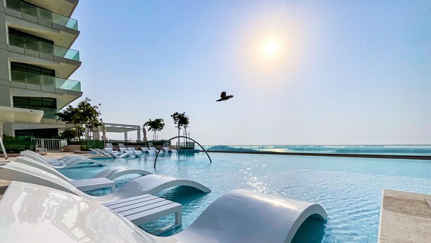 Ein Poolbereich mit modernen Liegestühlen, einem wolkenlosen Himmel und weiter Aussicht auf das Meer.