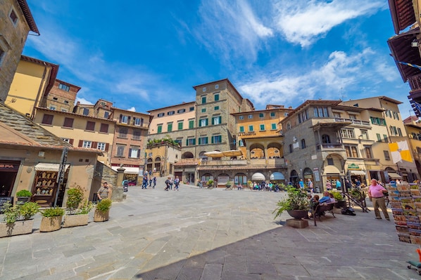 A historic square with stone buildings, outdoor seating, and a clear blue sky.