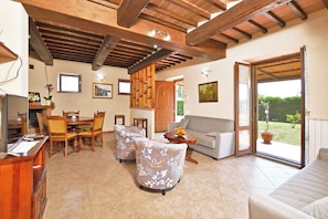Amplia sala de estar con techo de madera, un sofá, una mesa de comedor con sillas y un ventanal corredizo que da a un espacio exterior.