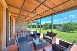 An outdoor patio with wicker furniture, a table, and a view of the garden.