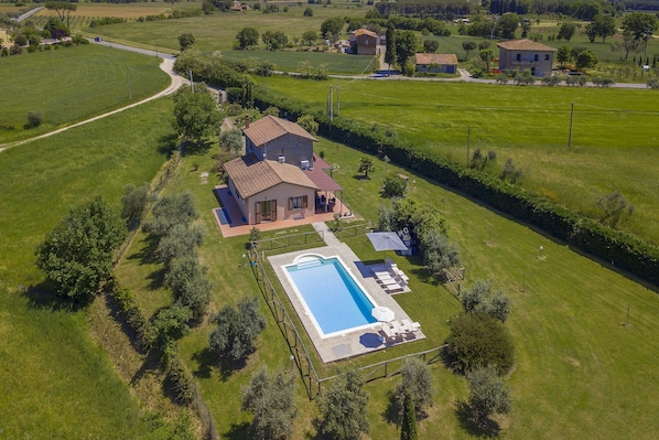 Vue aérienne d’une maison avec une piscine, entourée de champs verdoyants et d’arbres.