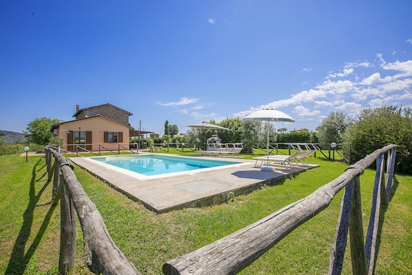 A swimming pool with a wooden fence, a house, and a clear blue sky.