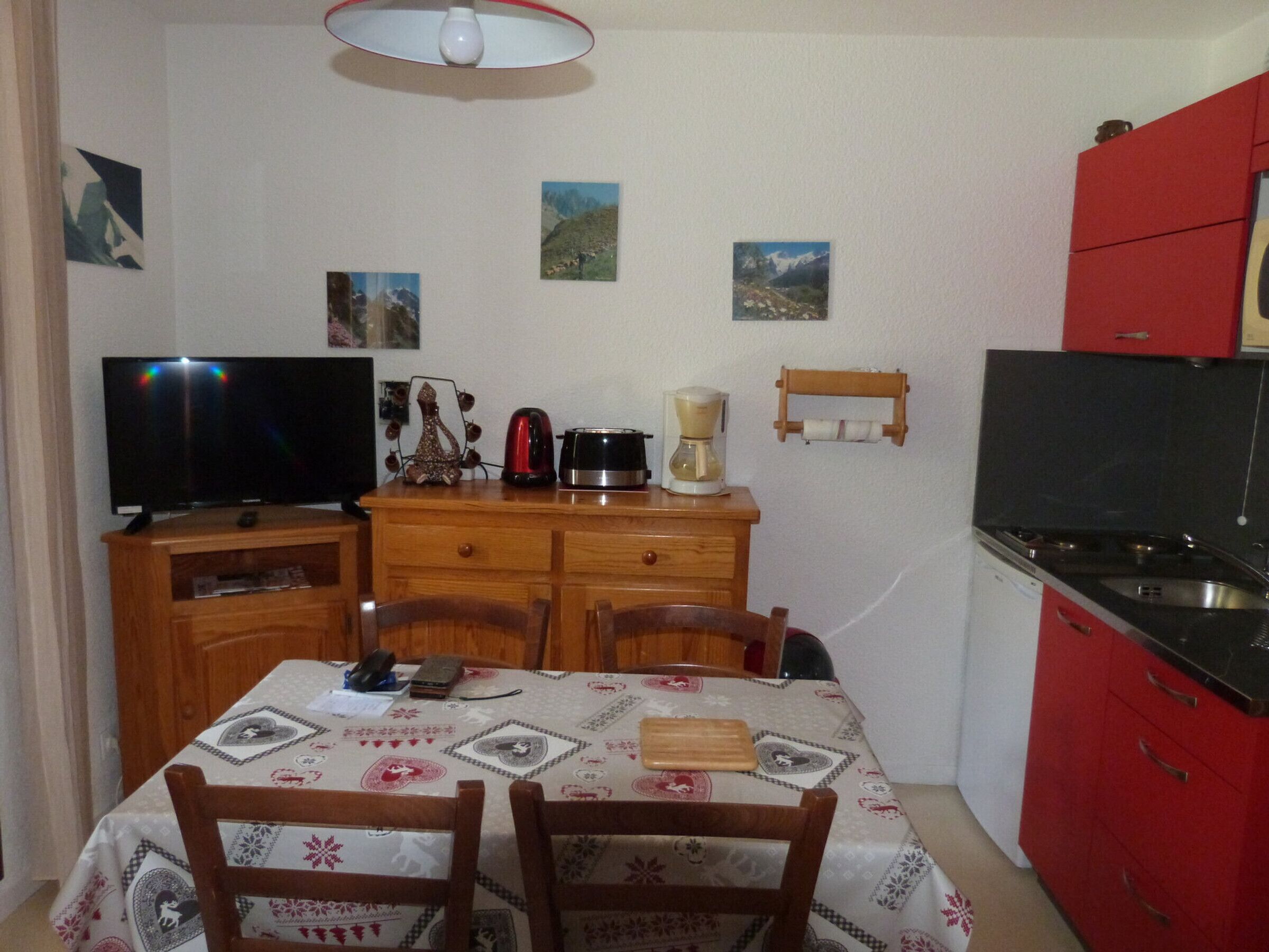 A compact kitchen with a dining table, chairs, a TV, a coffee maker, and a red cabinet.