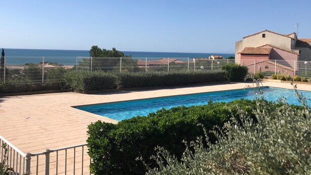 A swimming pool with a view of the sea, surrounded by a fence and greenery. - Cosy T2 sea view, bedroom + cabin, mezzanine, parking (Fleury)