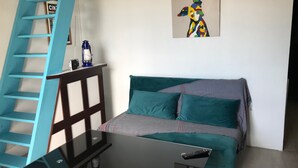 A bedroom with a bed, a desk, a chair, a ladder, a painting, and a window. - Cosy T2 sea view, bedroom + cabin, mezzanine, parking (Fleury)