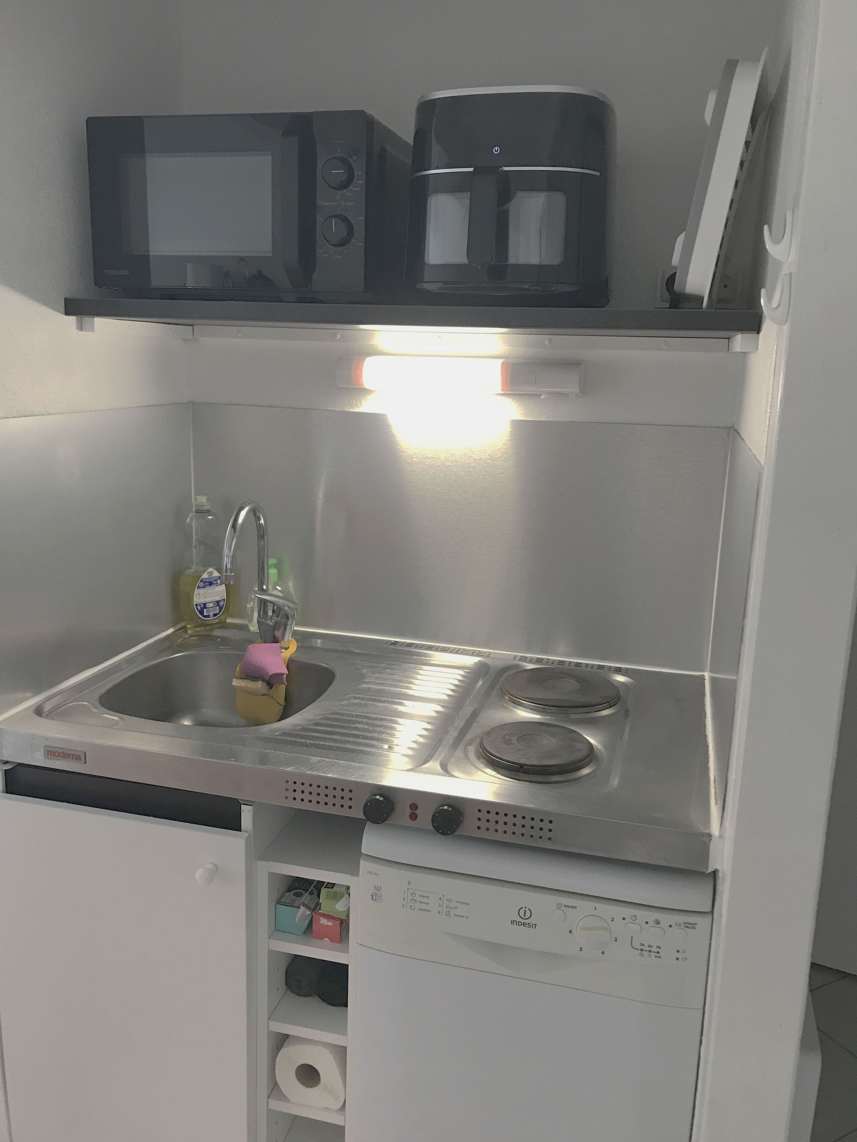 Ett kompakt kök med mikrovågsugn, kaffebryggare, diskho och diskmaskin.