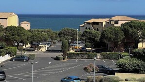 A coastal parking lot with cars, trees, and buildings. - Cosy T2 sea view, bedroom + cabin, mezzanine, parking (Fleury)
