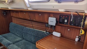 A cozy interior with a blue cushioned sofa, a wooden table with electronic devices, and a window. - 10 m boat in Morgat harbour (CROZON)