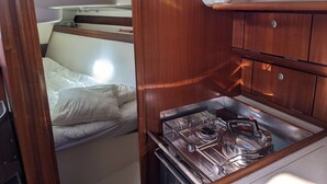 A compact RV interior with a bunk bed, a kitchenette with a stove and kettle, and a small storage cabinet. - 10 m boat in Morgat harbour (CROZON)