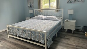 Une chambre à coucher comprenant un lit, deux tables de chevet, une fenêtre avec des rideaux et deux lampes fixées au mur.