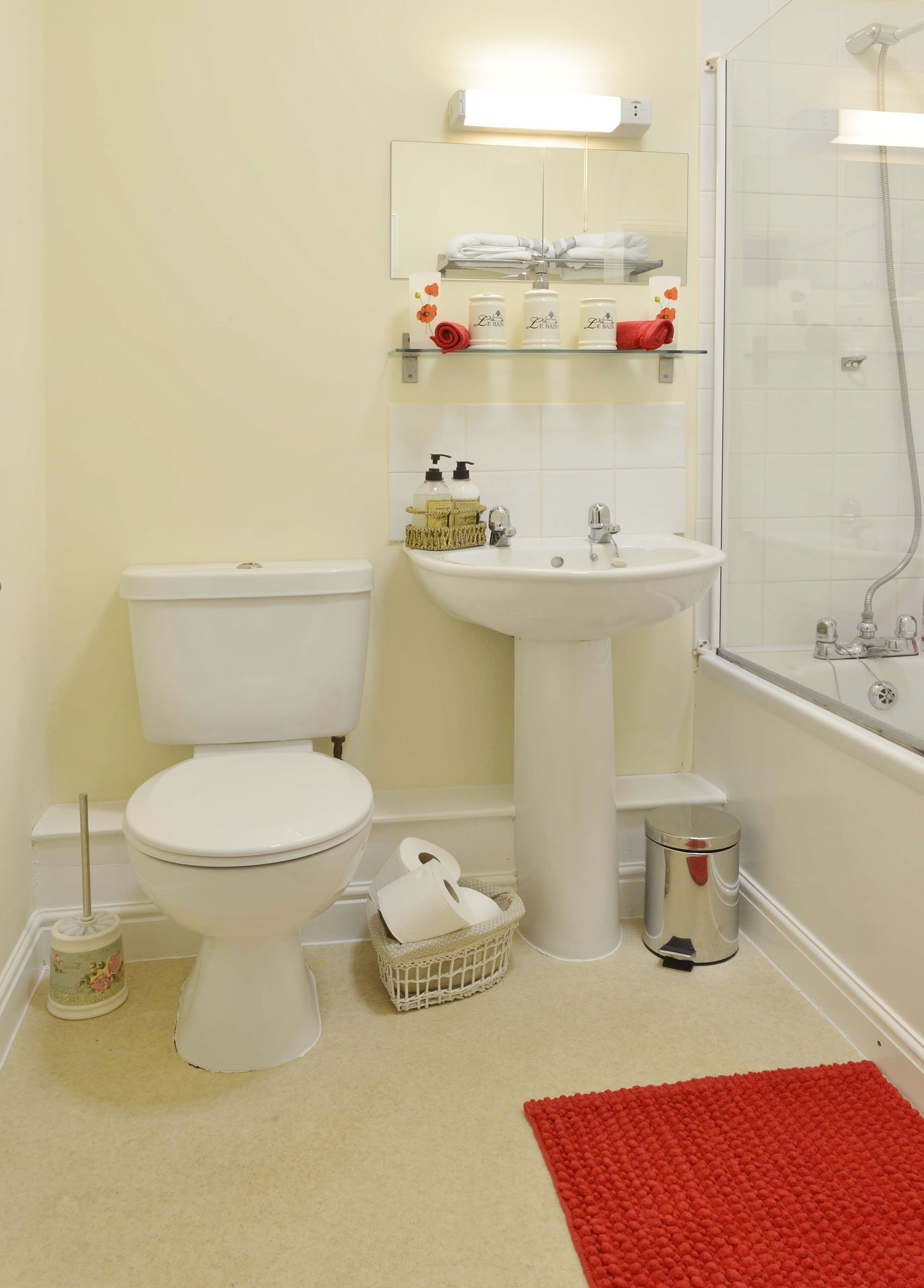 A bathroom with a toilet, sink, and shower. There are toiletries on the sink and a trash can.