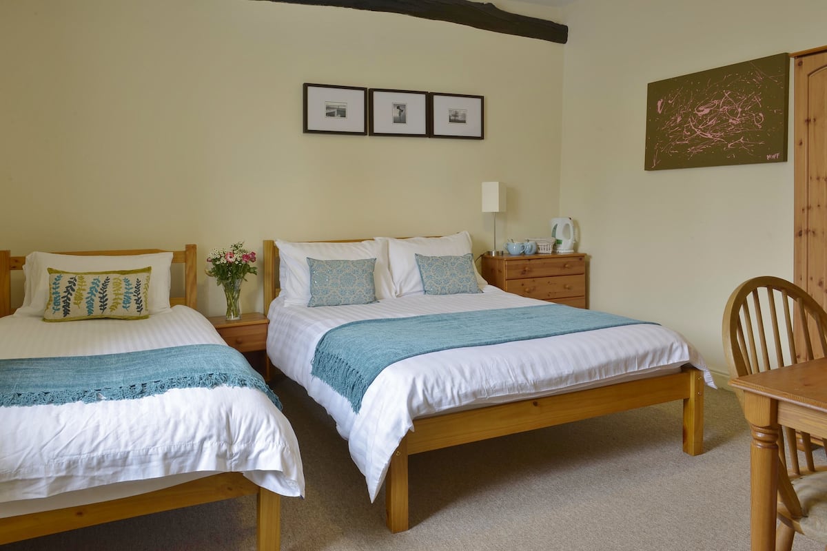 A bedroom with two wooden beds, a nightstand with a lamp, a chair, and a small table.