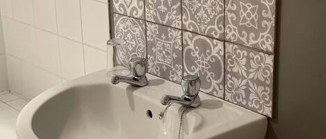 A bathroom with a white sink, two faucets, and a decorative tile backsplash.