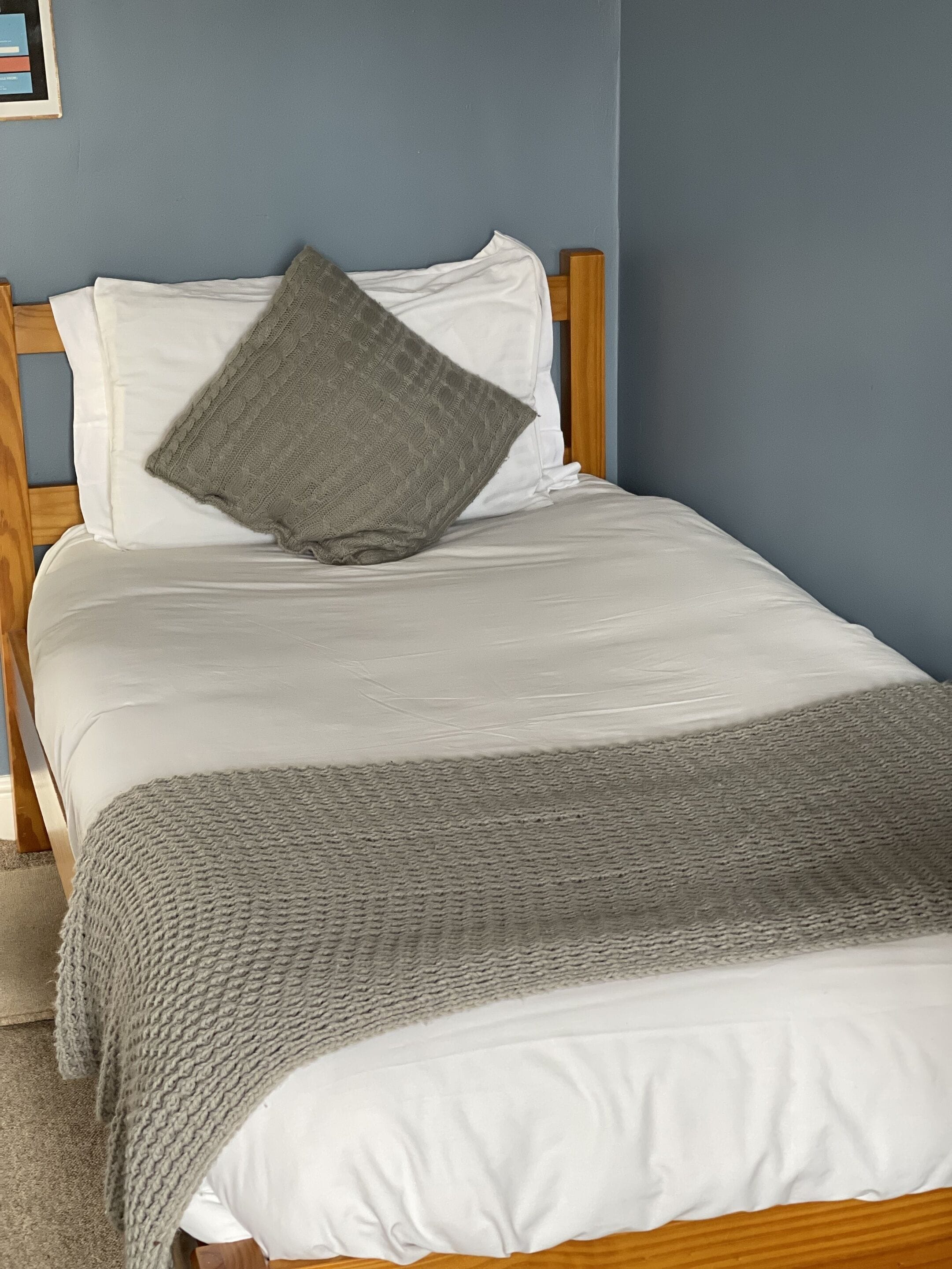 Una cama bien hecha con sábanas blancas y un plaid de punto gris.