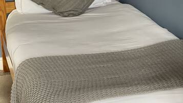 Una cama bien hecha con sábanas blancas y un plaid de punto gris.