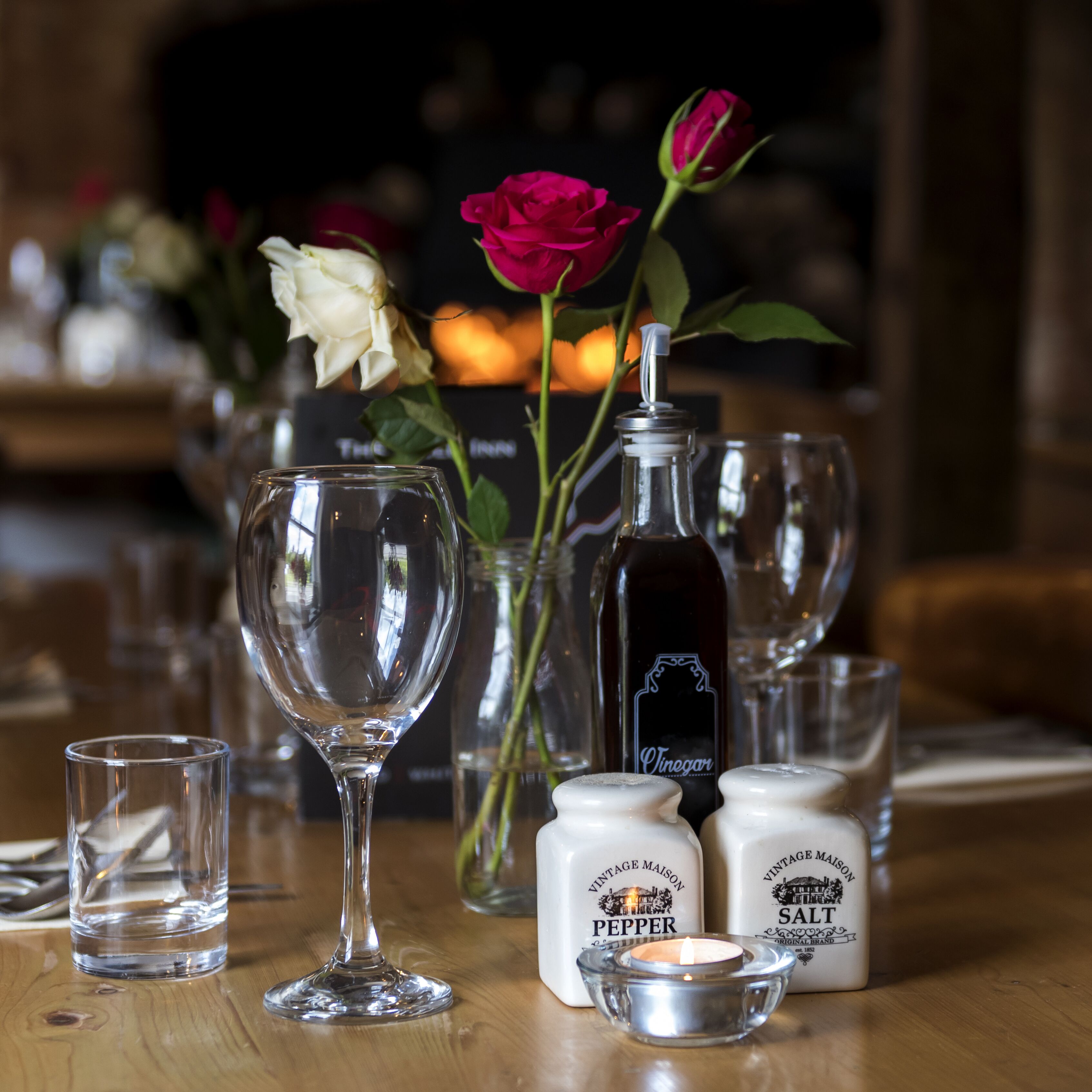 A table with a wine glass, a candle, salt and pepper shakers, and a bottle of vinegar.