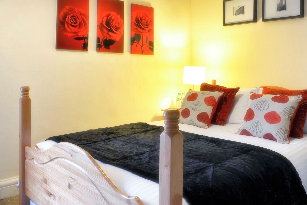 A bed with a wooden headboard, a black and white patterned pillow, and a red rose painting on the wall.