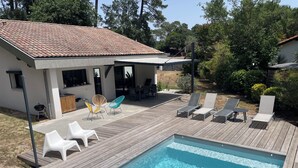 Zwembad met houten terras, ligstoelen en een patio met een barbecue.