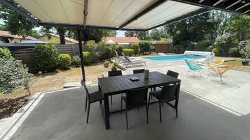 Eine überdachte Terrasse mit Pool, Gartenmöbeln und Blick auf den Garten.