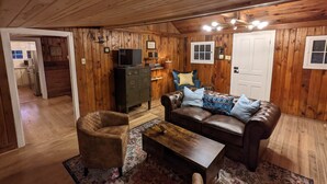 Ein gemütliches Zimmer mit Holzwänden, einem Ledersofa, einem Holztisch und einem Fernseher auf einem Schrank.