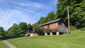 Eine rustikale Holzhütte mit Veranda, umgeben von üppigem Grün und blauem Himmel.