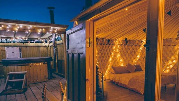 Ein gemütliches Blockhaus mit Holzfassade, einer Bar mit Lichterkette und einem Bett mit diamantmusteriger Wand und Lichterkette.