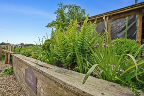 Een verhoogd houten plantenbak met een bord waarop staat 'Kruidentuin'.