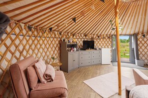 Een gezellig interieur van een joert met een comfortabele zithoek, een kleine tafel met een vaas, en een kast met diverse spullen.