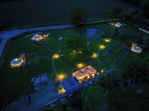 Luchtbeeld van een landgoed met meerdere jurten en een centraal gebouw, omgeven door een verzorgd gazon en paden.