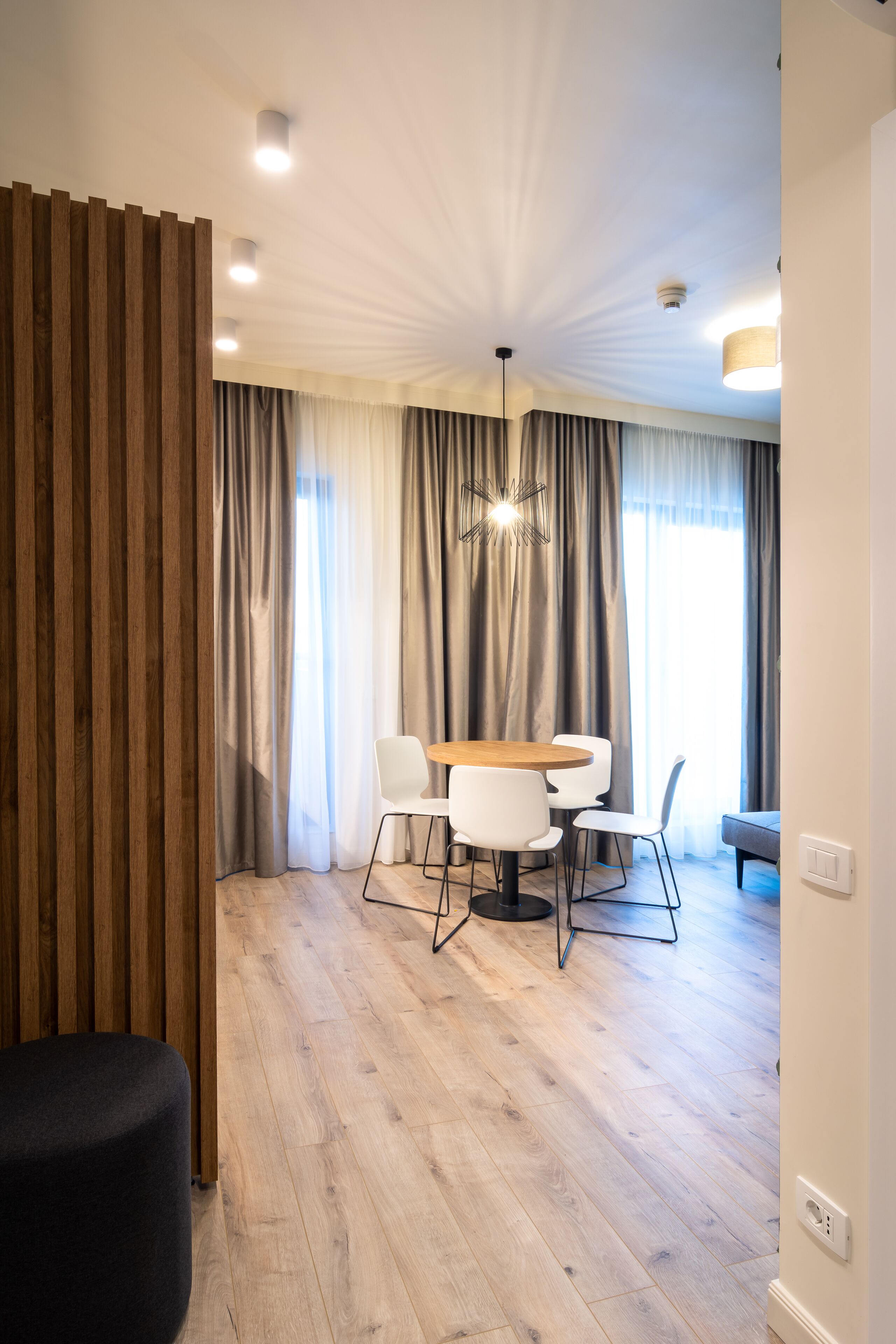 Un espace repas moderne avec une table et des chaises en bois, un pouf noir et un luminaire suspendu au plafond.