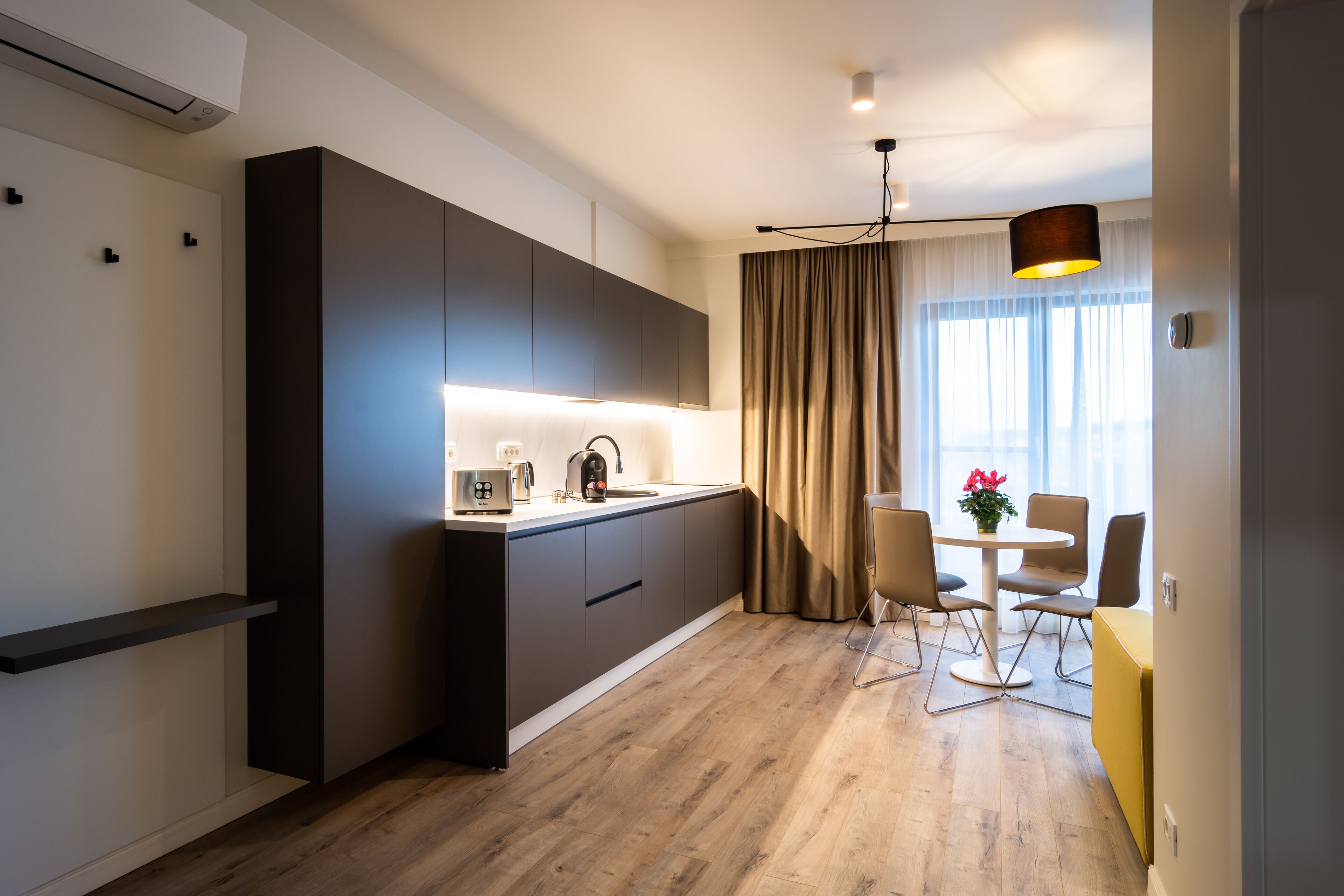 A modern kitchen with a built-in stove, a coffee maker, and a dining area with a table and chairs.