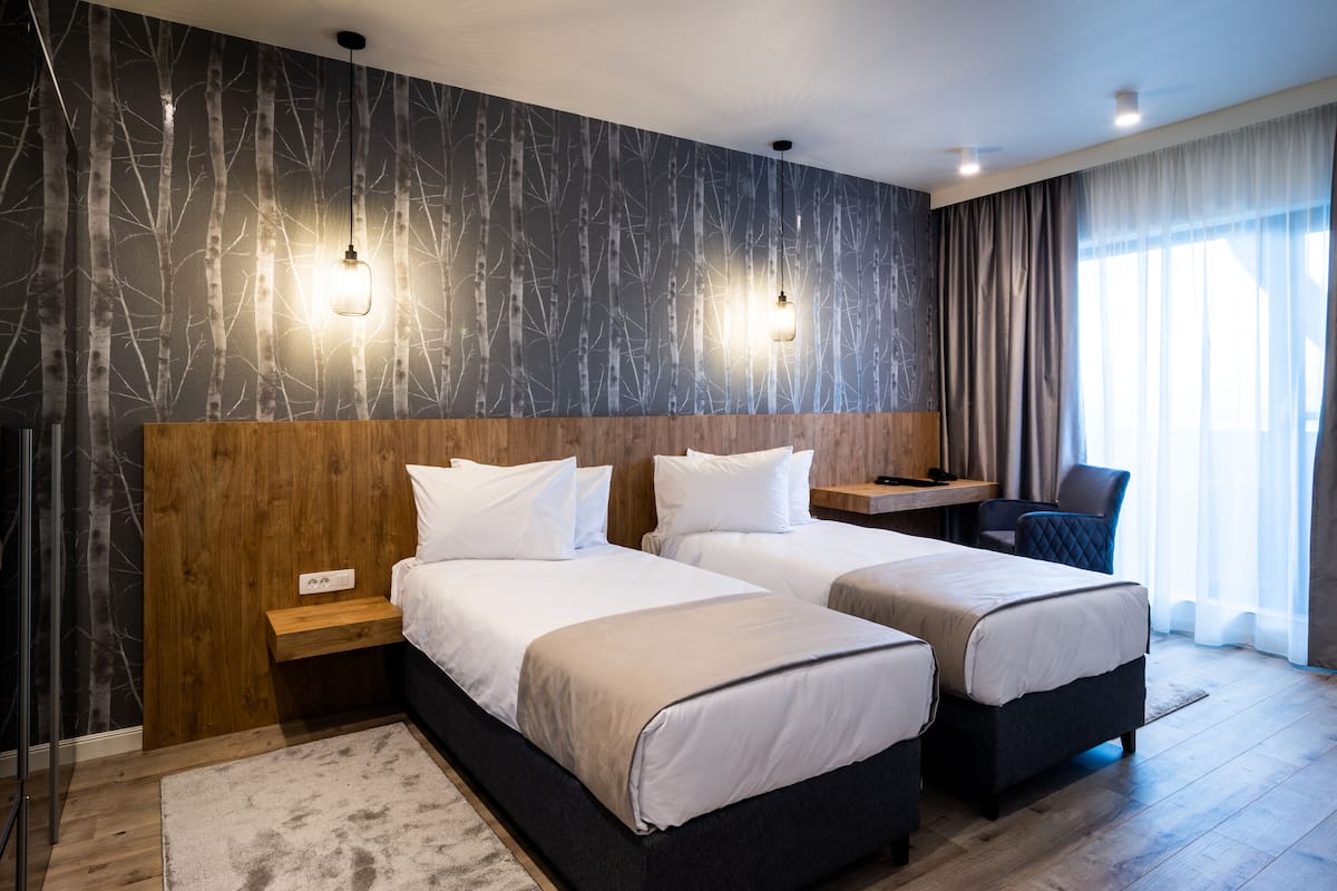 A hotel room with two beds, a wooden headboard, a desk, and a chair.