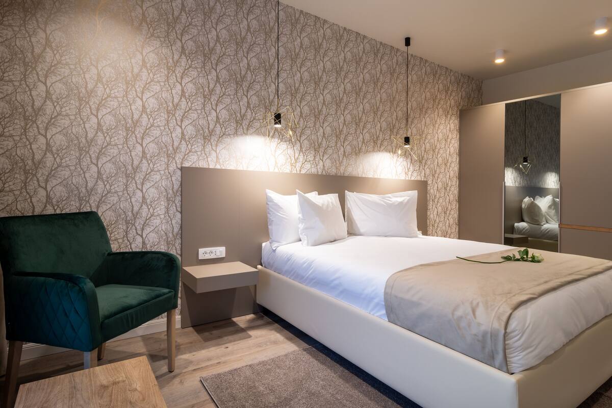 A modern bedroom with a large bed, a green armchair, and a nightstand.