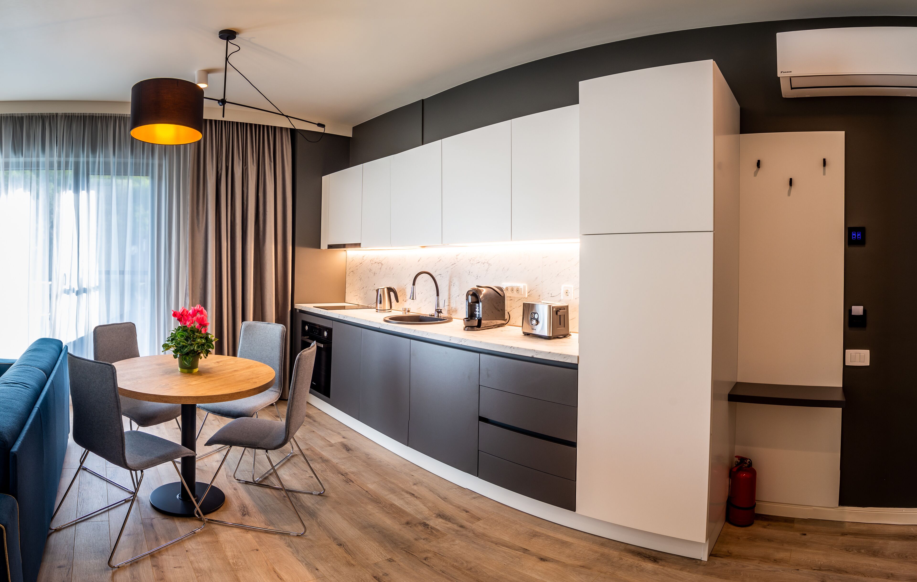 A modern kitchen with a round dining table, grey chairs, and a pendant light.