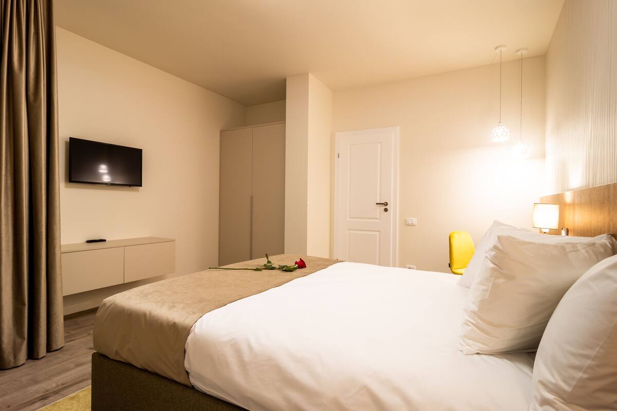 A hotel room with a bed, a TV mounted on the wall, a door, and a bedside table.