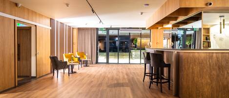 A modern hotel lobby with wooden flooring, a reception desk, and seating areas.