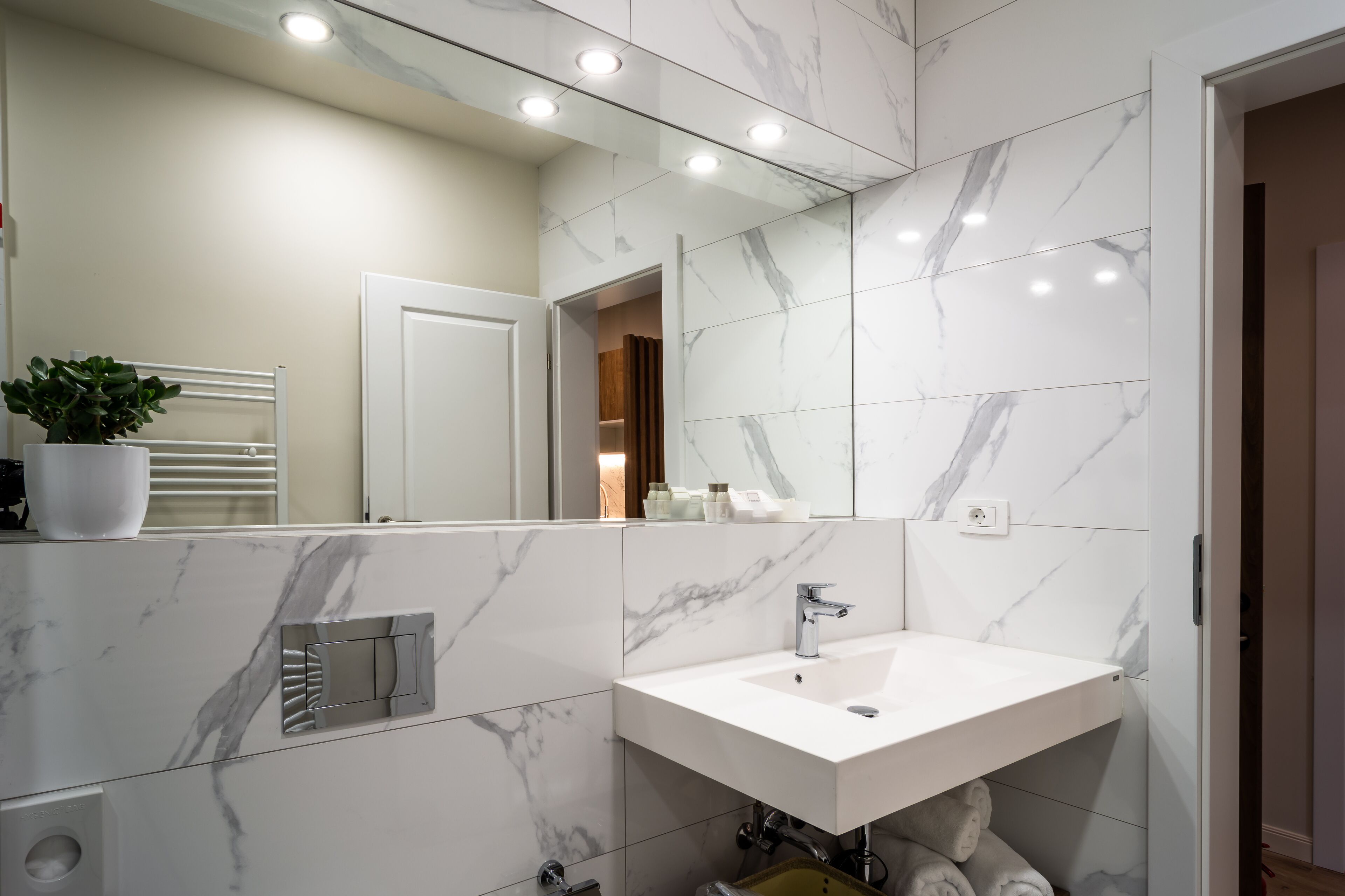A modern bathroom with a white marble sink, a large mirror, and a potted plant.