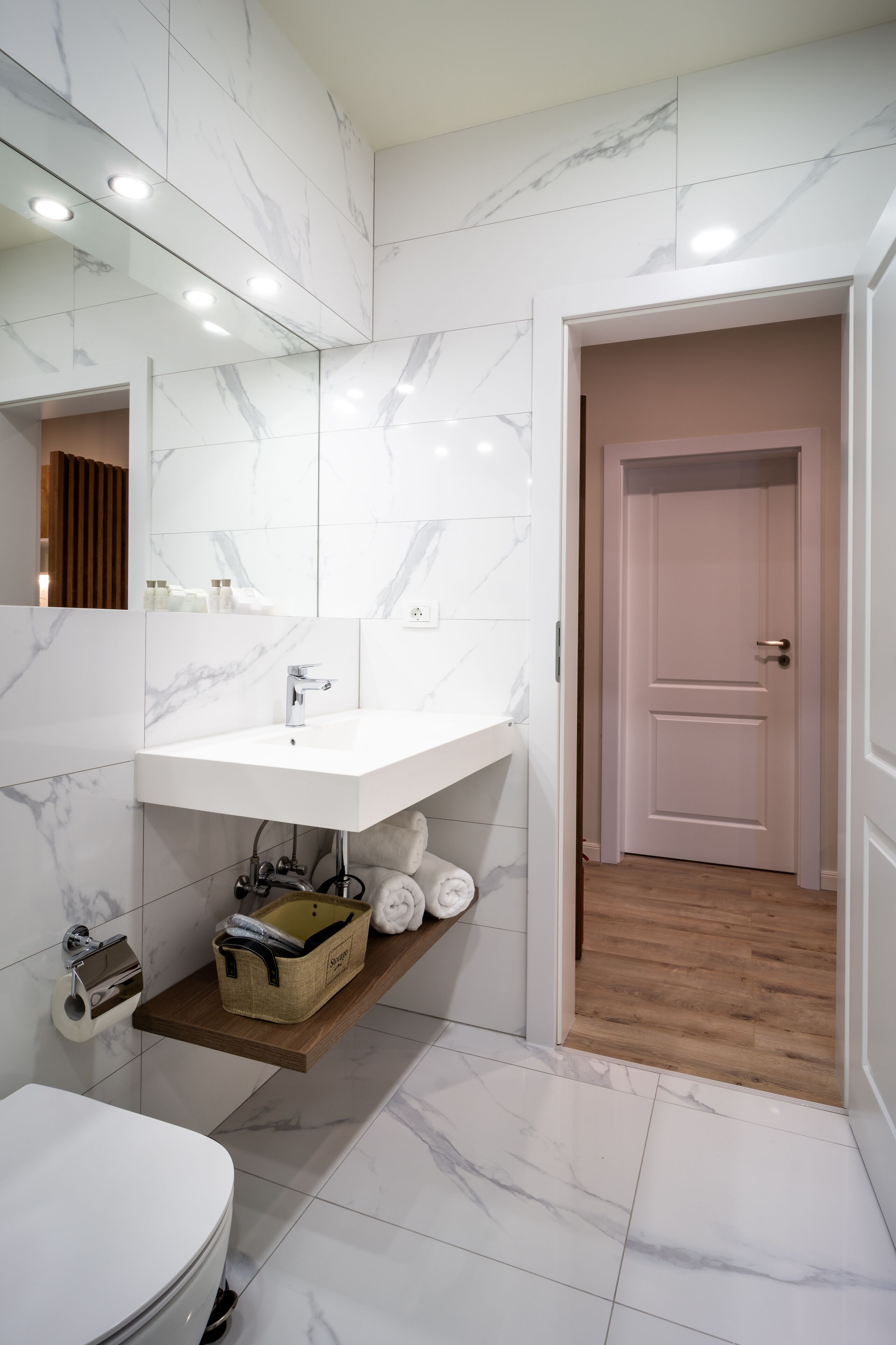 Un baño moderno con un lavamanos de mármol blanco, una estantería de madera y un inodoro blanco.