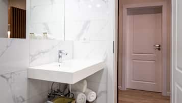 Un baño moderno con un lavamanos de mármol blanco, una estantería de madera y un inodoro blanco.