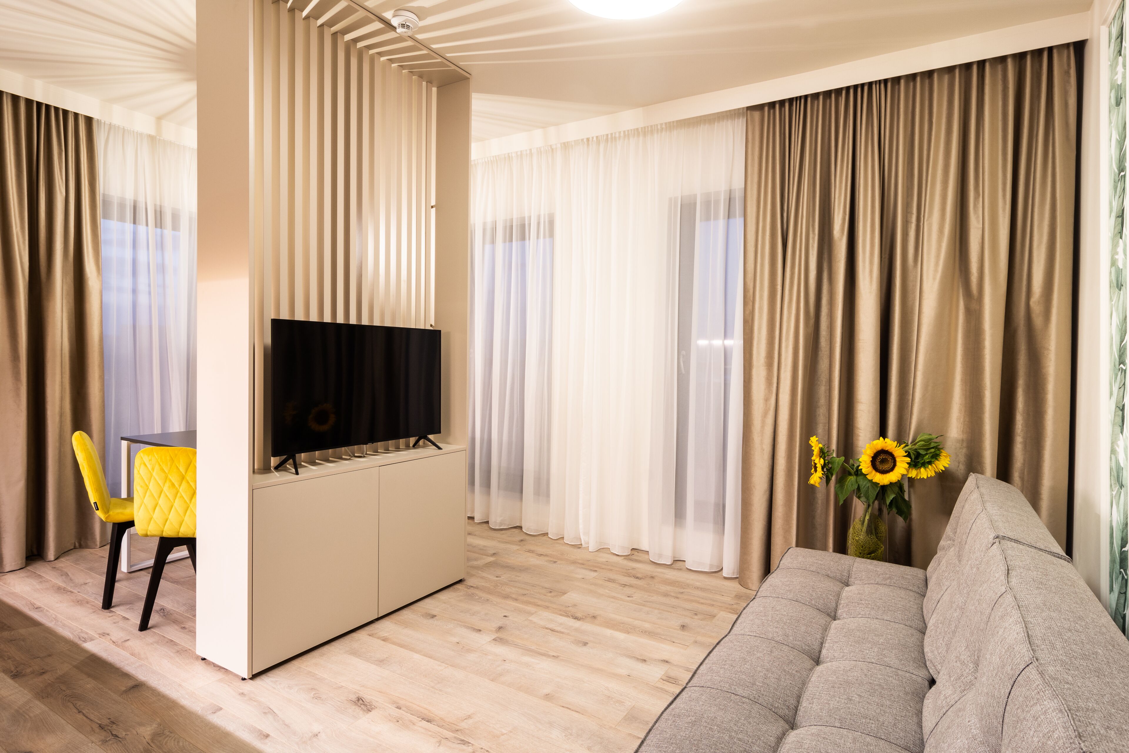Una sala moderna con un sofá, un televisor y una zona de comedor con una silla amarilla.