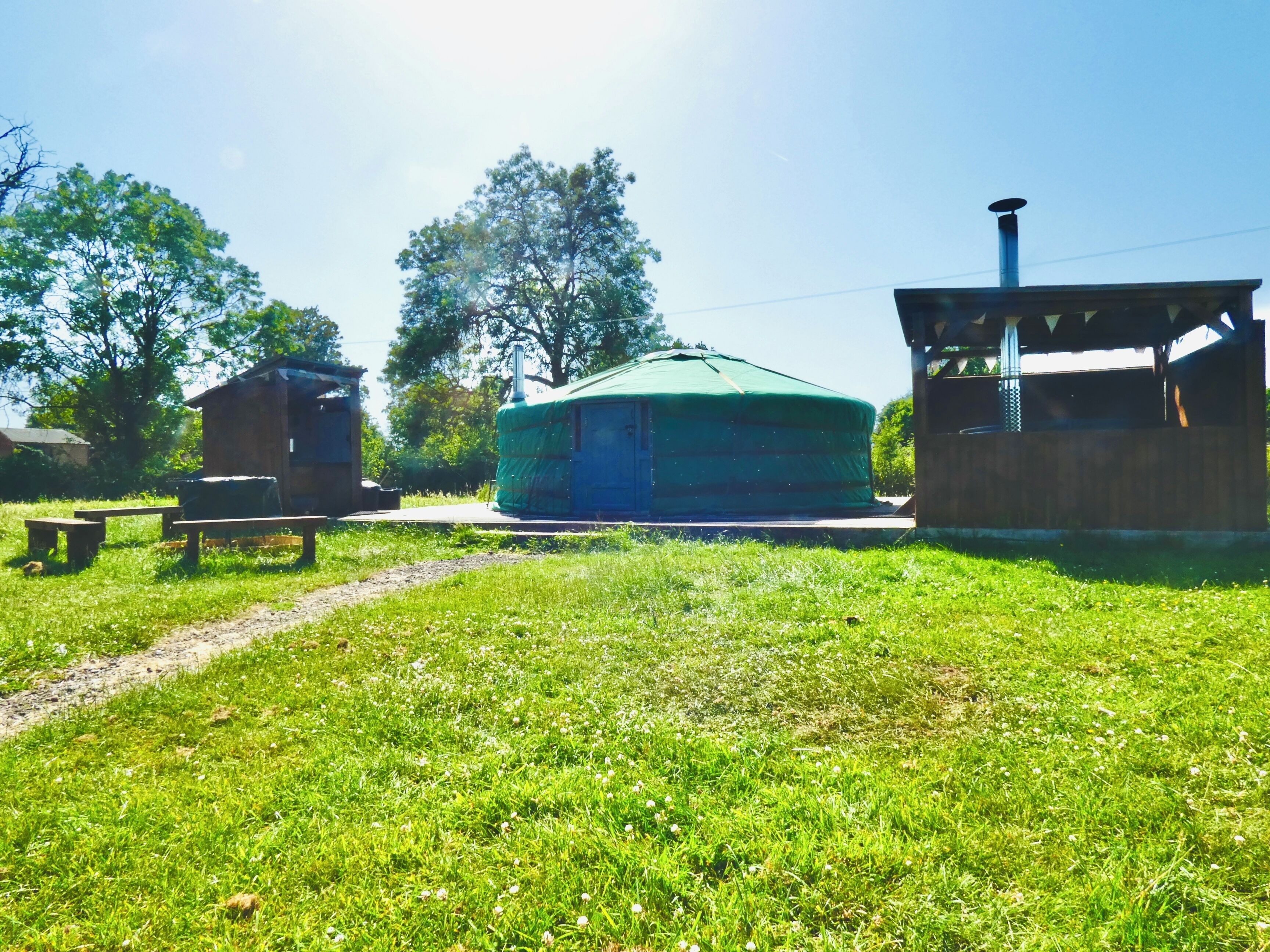 Une yourte avec un toit vert, une structure en bois sur la gauche et un petit bâtiment sur la droite.