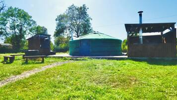 Une yourte avec un toit vert, une structure en bois sur la gauche et un petit bâtiment sur la droite.